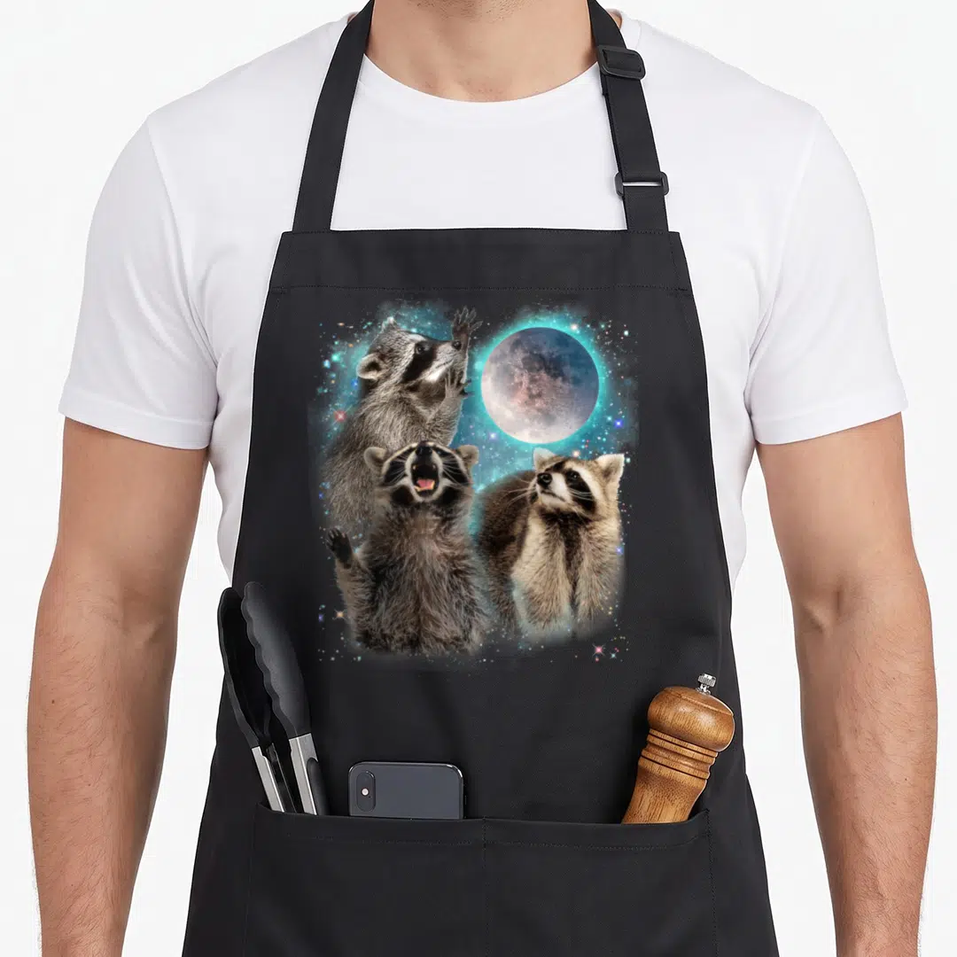 Raccoon cat dad apron - Three raccoons clustered under a full moon with grey, brown, and light blue stars — shown on a black cotton canvas apron against a white background