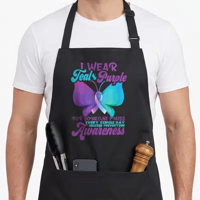 Funny awareness suicide prevention apron - Butterfly with ribbon body in purple and teal, surrounded by stacked — shown on a black cotton canvas apron against a white background