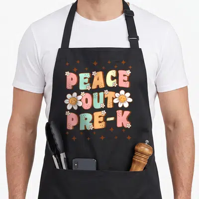 Peace preschool apron - Bubbly PEACE OUT PRE-K text with smiley daisies and brown stars — shown on a black cotton canvas apron against a white background