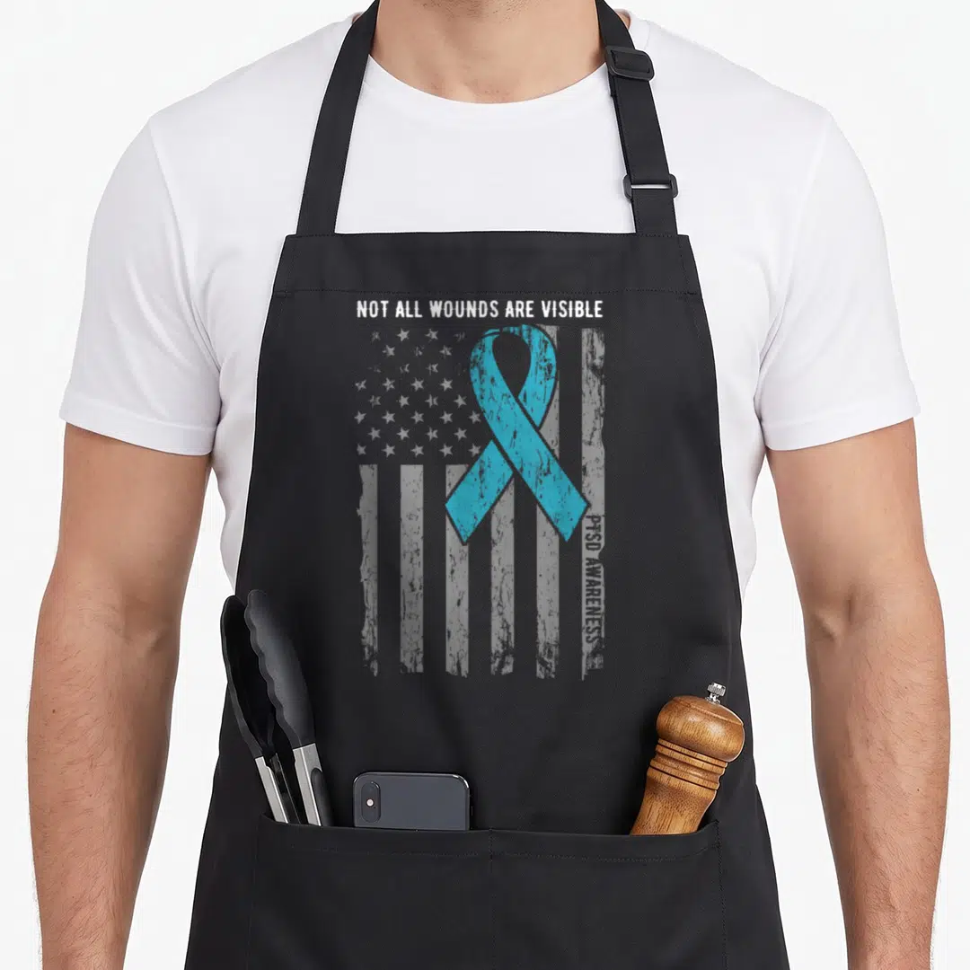 Wound us aprons - Teal ribbon over distressed white flag with visible wound text — shown on a black cotton canvas apron against a white background