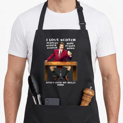 Anchorman scotch apron - Ron Burgundy in red suit at desk with I LOVE SCOTCH text and shorts visible — shown on a black cotton canvas apron against a white background