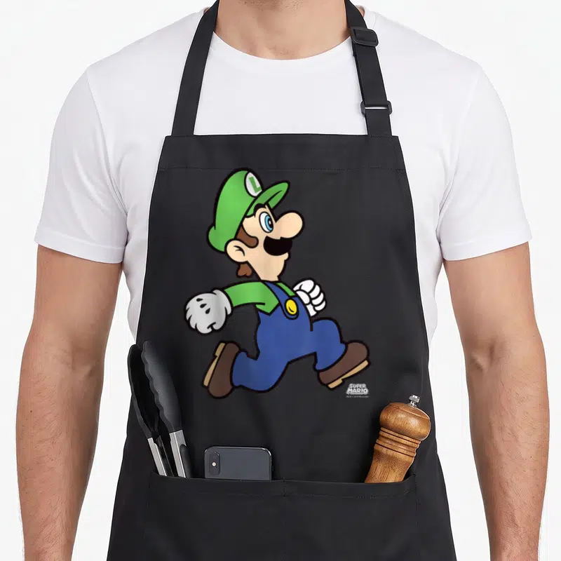 Run holiday apron - Luigi running in green and blue with SUPER MARIO logo text — shown on a black cotton canvas apron against a white background