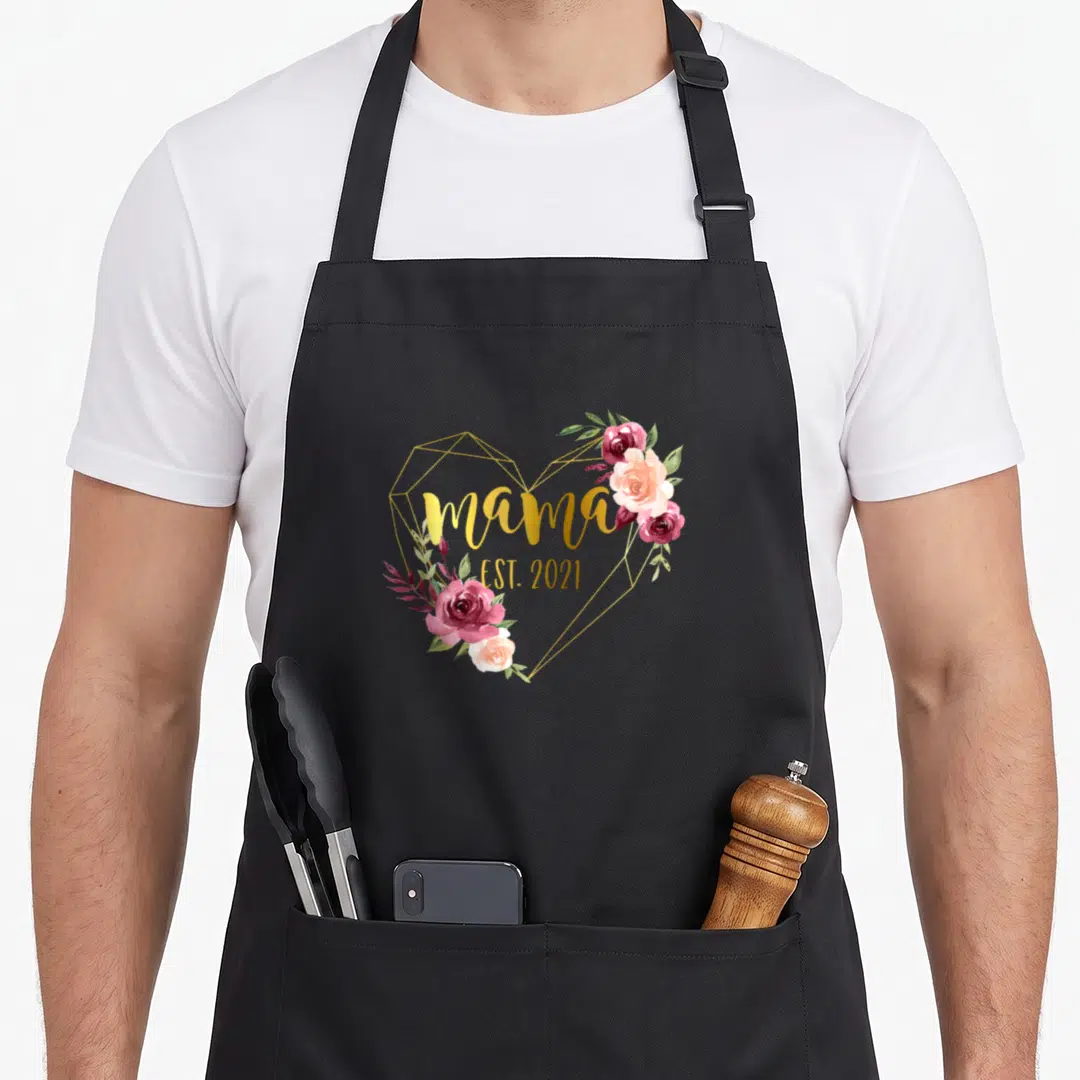 Baby mother's day aprons - Gold heart frame with watercolor roses and text mama EST 2021 — shown on a black cotton canvas apron against a white background
