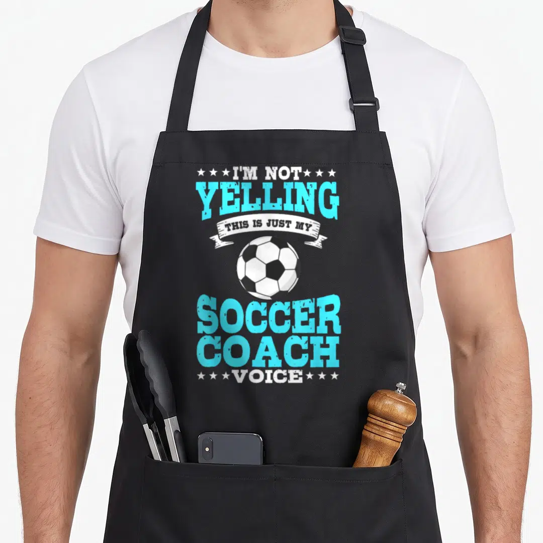 Soccer trainer dad apron - I'm Not Yelling Soccer Coach Voice text with ball and stars in white blue black — shown on a black cotton canvas apron against a white background