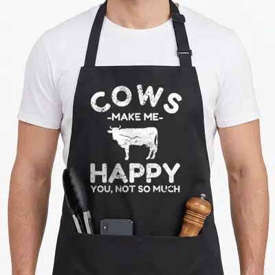 Vintage cow apron - White distressed text cows make me happy you not so much with cow silhouette — shown on a black cotton canvas apron against a white background