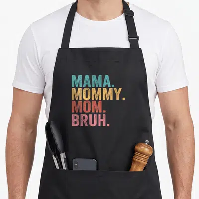 Mama bruh mother's day aprons - Stacked MAMA MOMMY MOM BRUH text in teal yellow orange pink colors — shown on a black cotton canvas apron against a white background