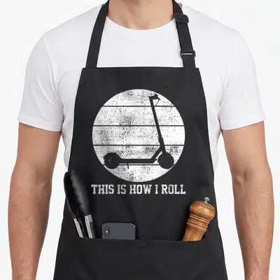 Electronic scooter apron - Grey scooter silhouette inside distressed white striped circle with text This Is How I Roll — shown on a black cotton canvas apron against a white background