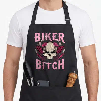 Biker rose apron - Pink BIKER BITCH text above skull with roses and shock absorbers — shown on a black cotton canvas apron against a white background