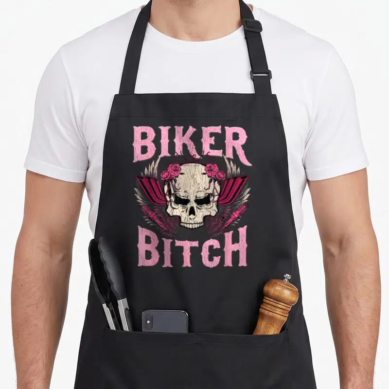 Biker rose apron - Pink BIKER BITCH text above skull with roses and shock absorbers — shown on a black cotton canvas apron against a white background