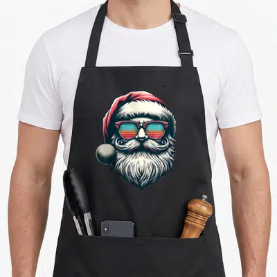 Sunglass christmas santa apron - Cartoon Santa with red hat, striped sunglasses, white beard, no text — shown on a black cotton canvas apron against a white background