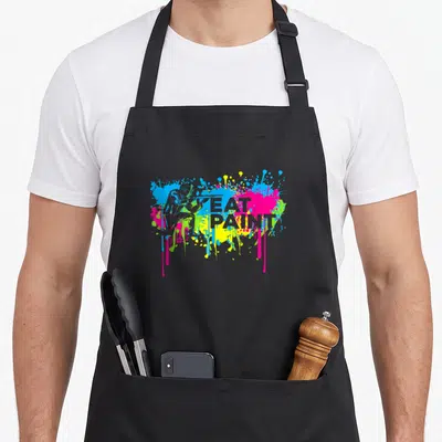 Paintball paint apron - EAT PAINT text over blue pink yellow green and white paint splatters and drips — shown on a black cotton canvas apron against a white background
