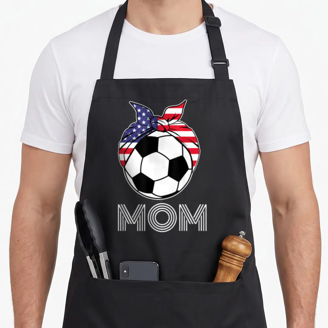 Soccer hair apron - Cartoon soccer ball with US flag bandana and MOM text — shown on a black cotton canvas apron against a white background