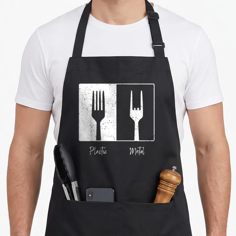 Hard punk rock apron - Minimalist graphic of two forks labeled plastic and metal in white and grey — shown on a black cotton canvas apron against a white background