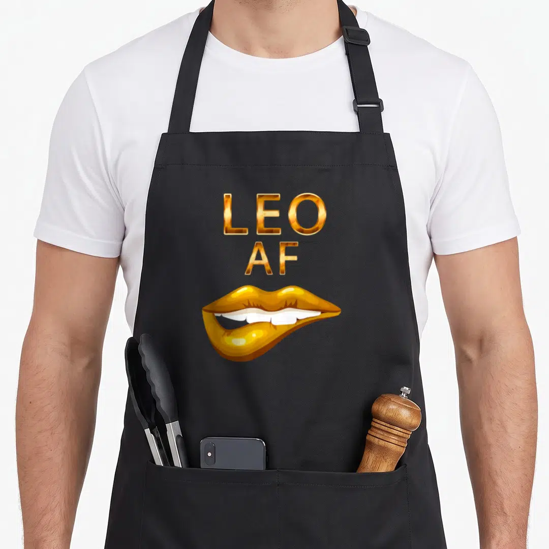 Leo lip birthday apron - Gold LEO AF text above metallic lips with white teeth — shown on a black cotton canvas apron against a white background