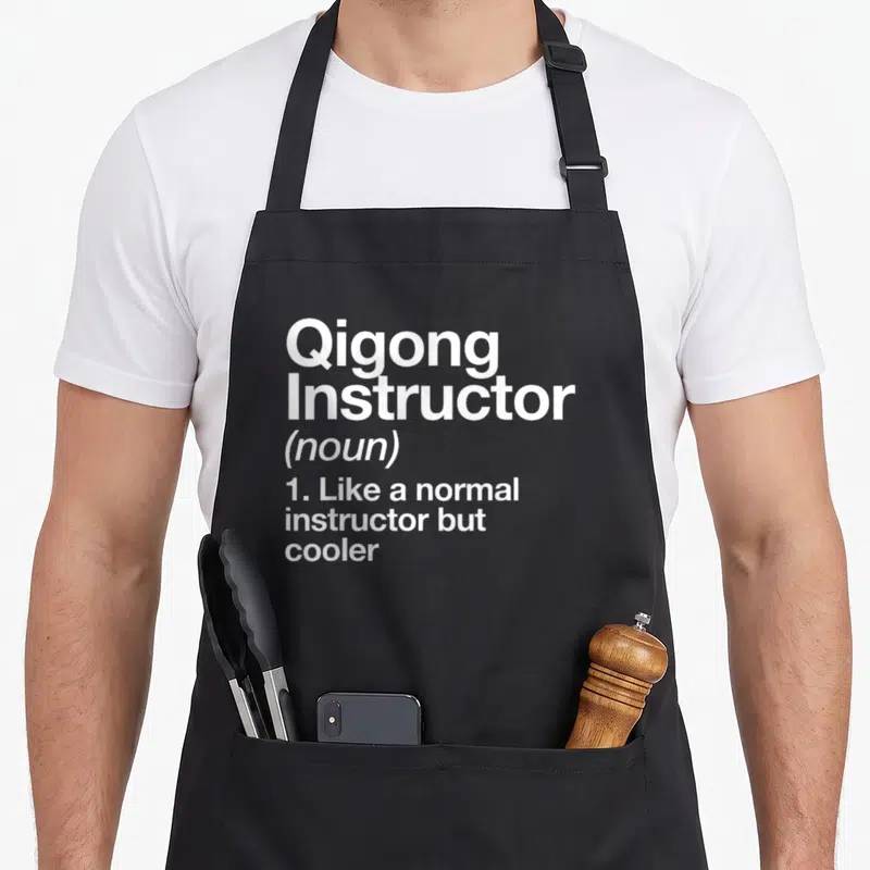 Instructor qigong apron - White text reading Qigong Instructor noun like normal but cooler on black background — shown on a black cotton canvas apron against a white background