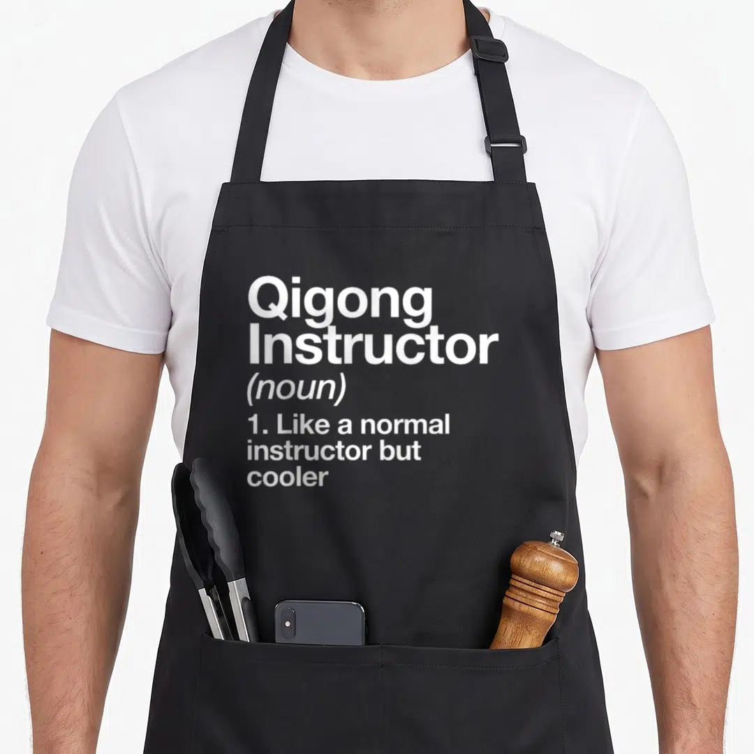 Instructor qigong apron - White text reading Qigong Instructor noun like normal but cooler on black background — shown on a black cotton canvas apron against a white background