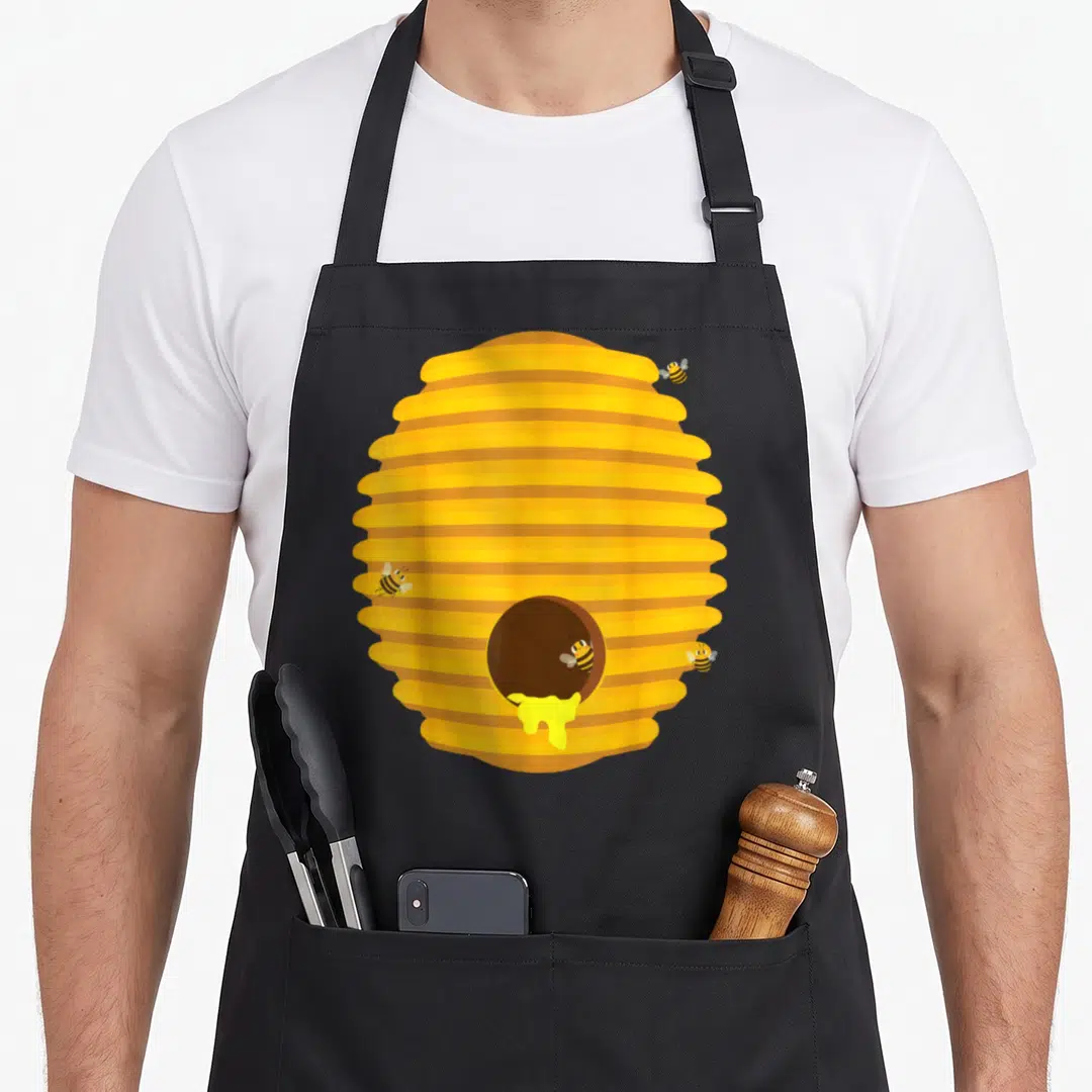 Beehive easy apron - Cartoon yellow and orange beehive with three flying bees and dripping honey on a black background — shown on a black cotton canvas apron against a white background