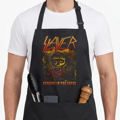 Season slayer apron - Distressed monster face and tombstones in orange and red with text SLAYER SEASONS IN THE ABYSS — shown on a black cotton canvas apron against a white background