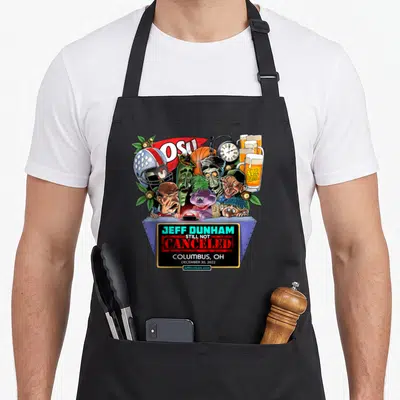 Jeff columbus apron - Caricature faces above sign reading Jeff Dunham Still Not Canceled Columbus OH Dec 30 2022 — shown on a black cotton canvas apron against a white background