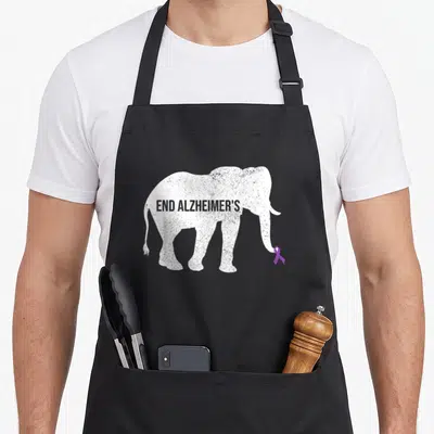 End alzheimer's aprons - Distressed white elephant silhouette holding purple ribbon with text END ALZHEIMER'S across — shown on a black cotton canvas apron against a white background