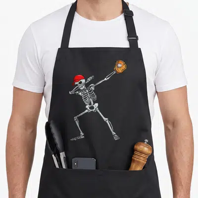 Skeleton baseball halloween apron - Cartoon skeleton in red cap and orange glove pitching a ball in a grey illustration — shown on a black cotton canvas apron against a white background
