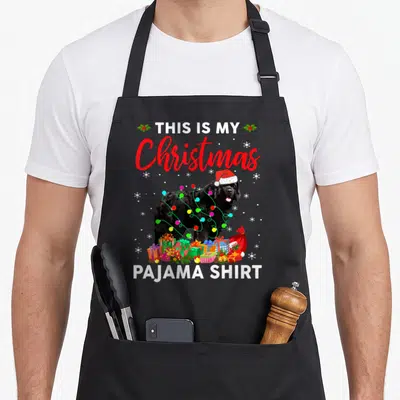 Newfoundland christmas dog apron - Black dog with Santa hat and lights behind gifts reading This Is My Christmas Pajama — shown on a black cotton canvas apron against a white background