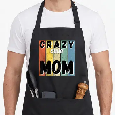 Chug cooking with dog apron - Retro stacked text CRAZY CHUG MOM over five vertical colored stripes — shown on a black cotton canvas apron against a white background