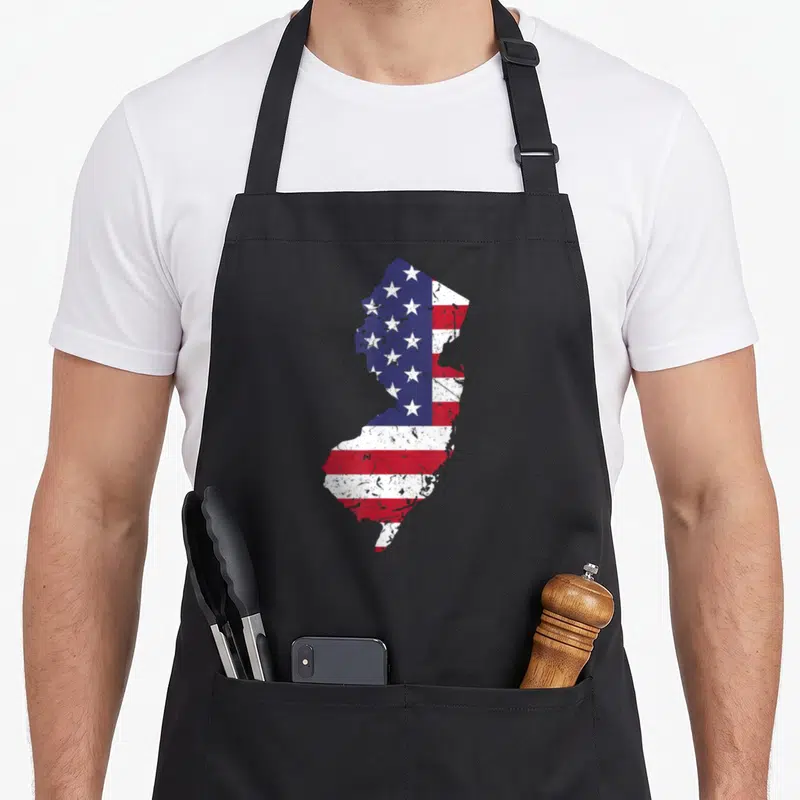 Jersey map 4th of july apron - New Jersey state map silhouette filled with distressed red white and blue American flag — shown on a black cotton canvas apron against a white background