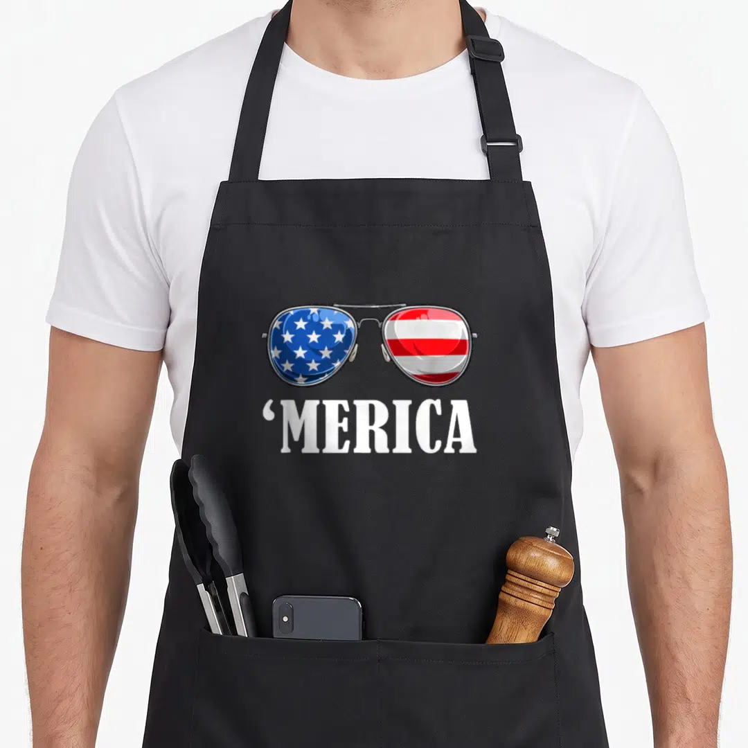 Independence patriot 4th of july apron - Sunglasses with flag lenses and MERICA text below — shown on a black cotton canvas apron against a white background