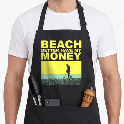 Cute detectorist metal detecting apron - Yellow text BEACH BETTER HAVE MY MONEY above man silhouette on yellow sky — shown on a black cotton canvas apron against a white background