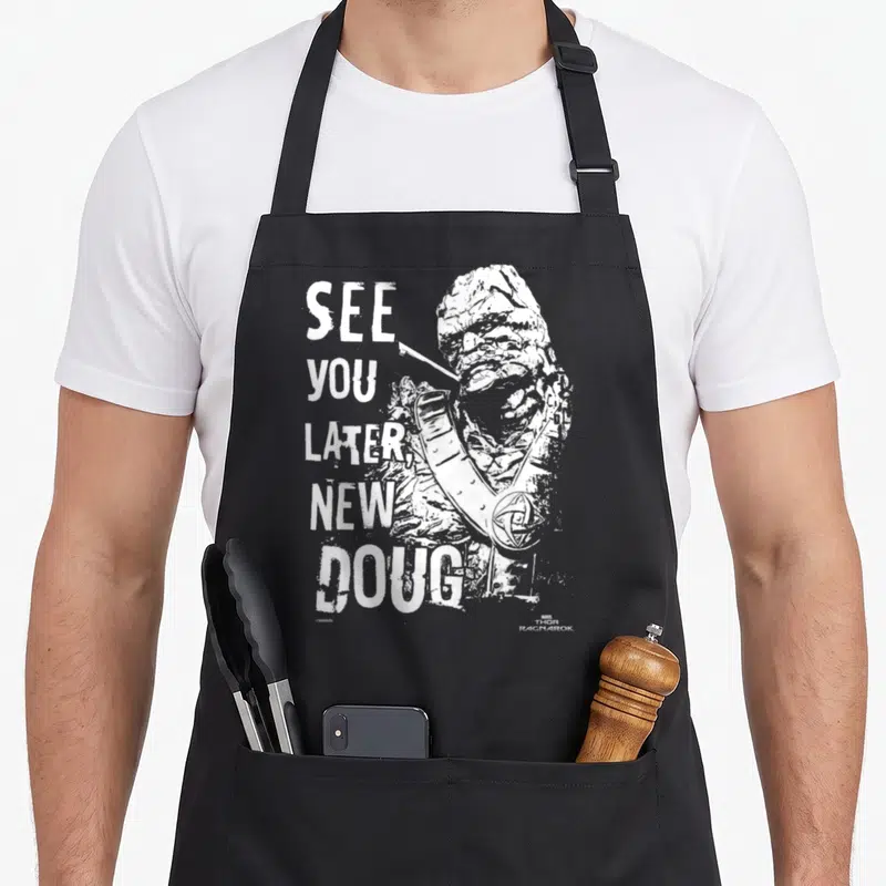 Ragnarok crew neck apron - White distressed text SEE YOU LATER NEW DOUG next to rocky character Korg — shown on a black cotton canvas apron against a white background