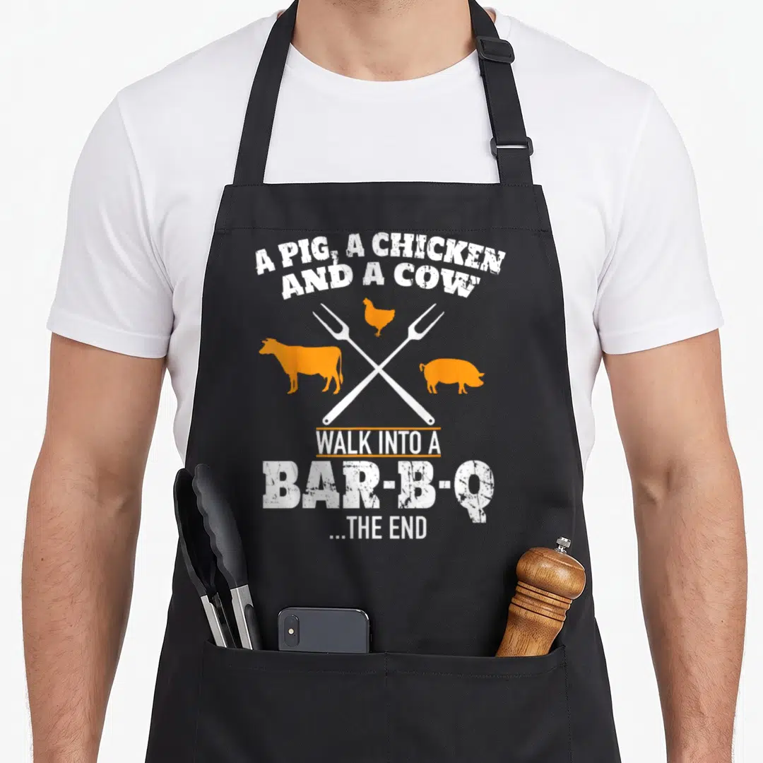 Scout cow apron - Distressed white text and orange pig chicken cow silhouettes over crossed forks — shown on a black cotton canvas apron against a white background
