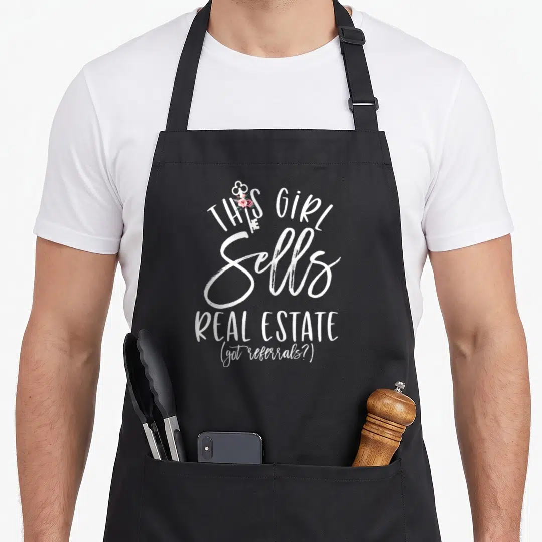 Estate floral apron - White key with pink roses and script text 'This Girl Sells Real Estate' — shown on a black cotton canvas apron against a white background