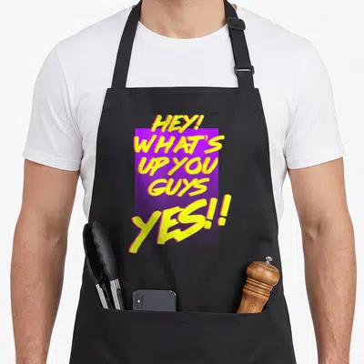 Shane dawson hey novelty apron - Yellow text HEY WHAT'S UP YOU GUYS YES!! on purple rectangle — shown on a black cotton canvas apron against a white background