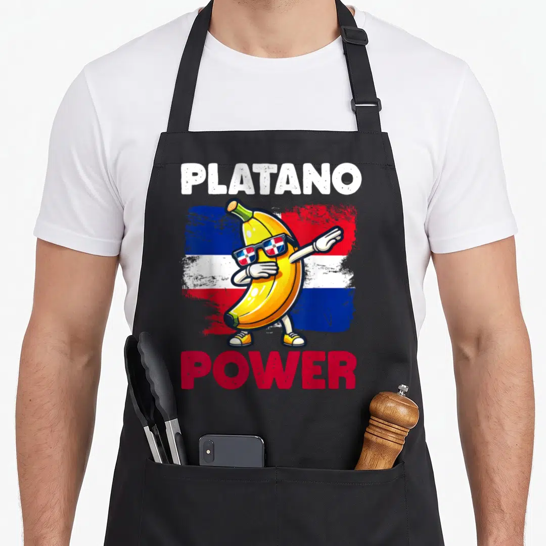 Platano dominican apron - Dabbing banana wearing flag sunglasses with PLATANO POWER text — shown on a black cotton canvas apron against a white background