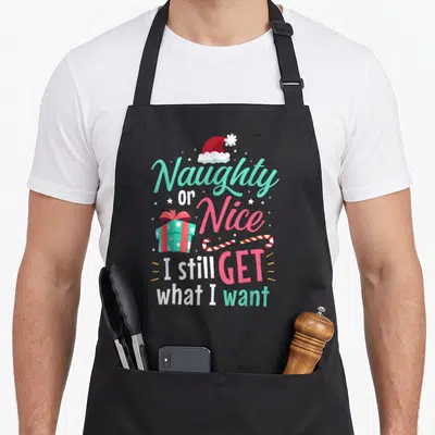 Cheeky womens christmas aprons - Santa hat, gift box, candy canes, and Naughty Nice text in teal and pink — shown on a black cotton canvas apron against a white background