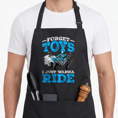 Forget atv apron - Blue cartoon ATV rider with smoke and text FORGET TOYS I JUST WANNA RIDE — shown on a black cotton canvas apron against a white background