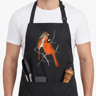 Funny bird cardinal apron - Two realistic cardinals in red and brown perched on a thorny grey branch — shown on a black cotton canvas apron against a white background