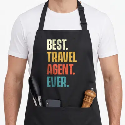 Agency travel aprons - Stacked text best travel agent ever in cream yellow red and blue block letters — shown on a black cotton canvas apron against a white background