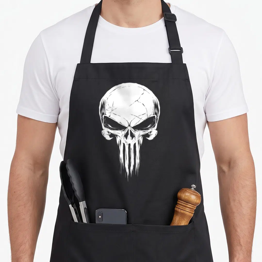 Punisher distressed apron - White stylized skull with cracked forehead and dripping jaw printed on grey background — shown on a black cotton canvas apron against a white background