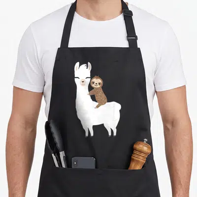 Sloth birthday apron - White llama with brown sloth clinging to back in cartoon style — shown on a black cotton canvas apron against a white background