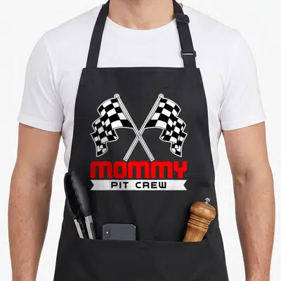 Pit racing crew aprons - Crossed checkered flags above red MOMMY text and white PIT CREW banner — shown on a black cotton canvas apron against a white background