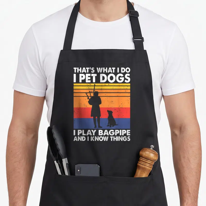 Play dog apron - Retro bagpiper and dog silhouette with white text on yellow orange red blue stripes — shown on a black cotton canvas apron against a white background