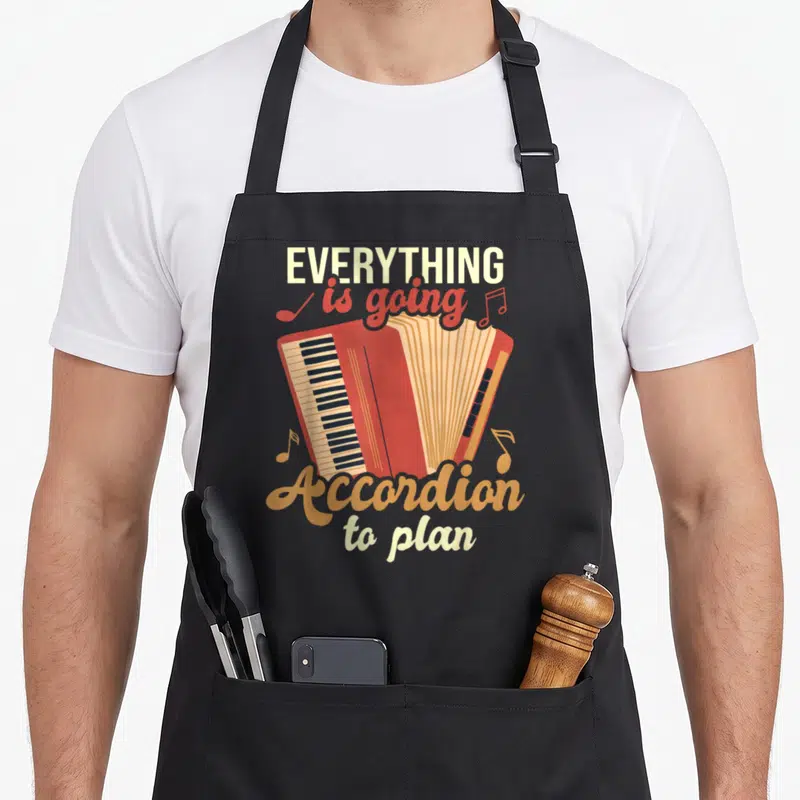 Accordion cumbia apron - Red cartoon accordion with scattered notes and text EVERYTHING is going Accordion to plan — shown on a black cotton canvas apron against a white background