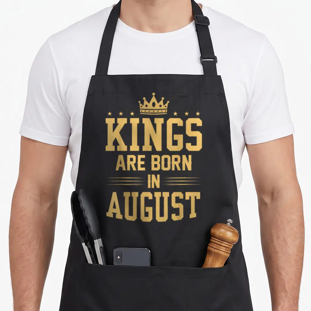 August king apron - Gold crown and six stars above stacked Kings are born in August text — shown on a black cotton canvas apron against a white background