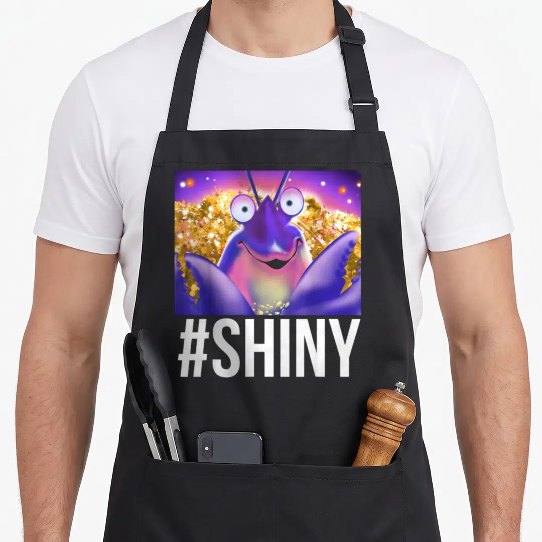 Shiny novelty apron - Cartoon purple insect in gold glitter square with #SHINY text below — shown on a black cotton canvas apron against a white background