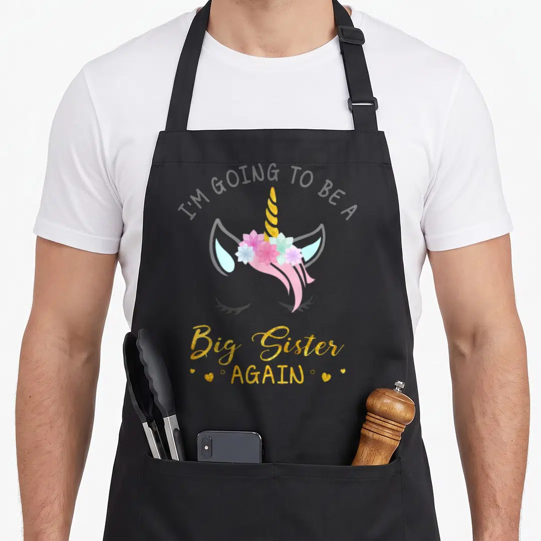 Funny sister unicorn apron - Unicorn head with gold horn pink mane flowers and text I'M GOING TO BE A Big Sister AGAIN — shown on a black cotton canvas apron against a white background