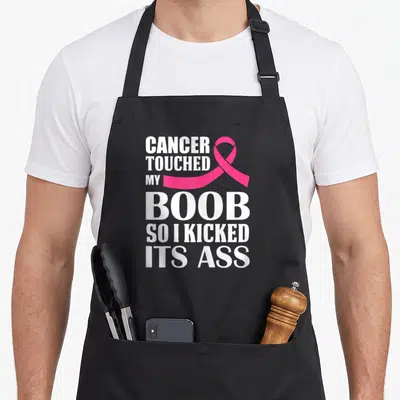 Touched breast cancer awareness aprons - White text reading Cancer Touched My Boob So I Kicked Its Ass next to a pink — shown on a black cotton canvas apron against a white background