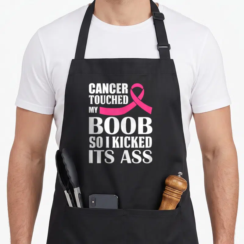 Touched breast cancer awareness aprons - White text reading Cancer Touched My Boob So I Kicked Its Ass next to a pink — shown on a black cotton canvas apron against a white background