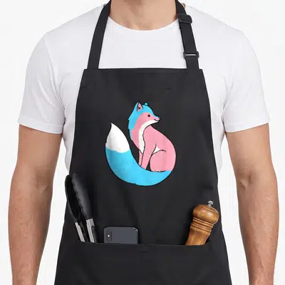 Tran fox print apron - Cartoon fox in blue pink and white transgender pride colors — shown on a black cotton canvas apron against a white background